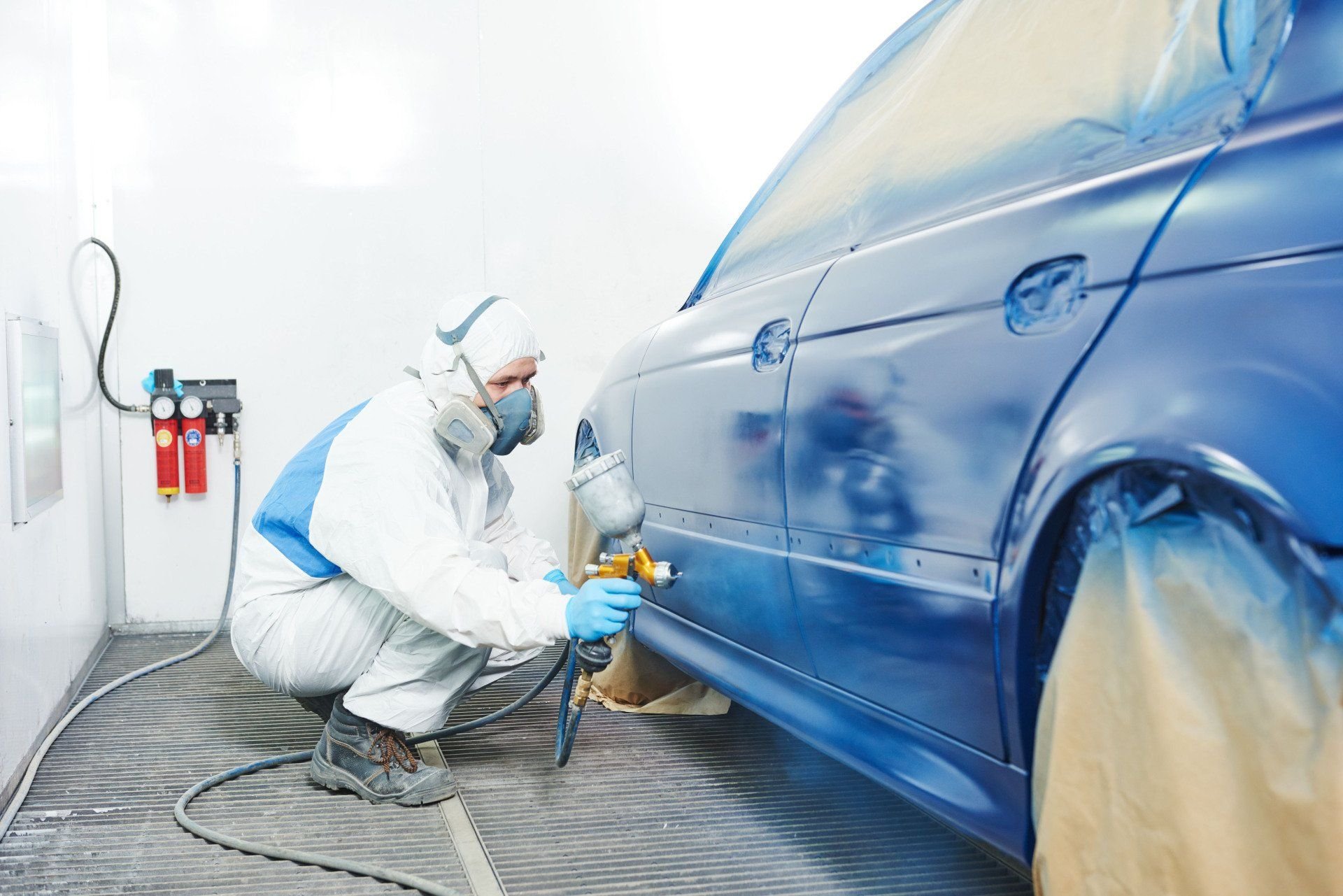 A technician refinishing a blue vehicle in a paint booth